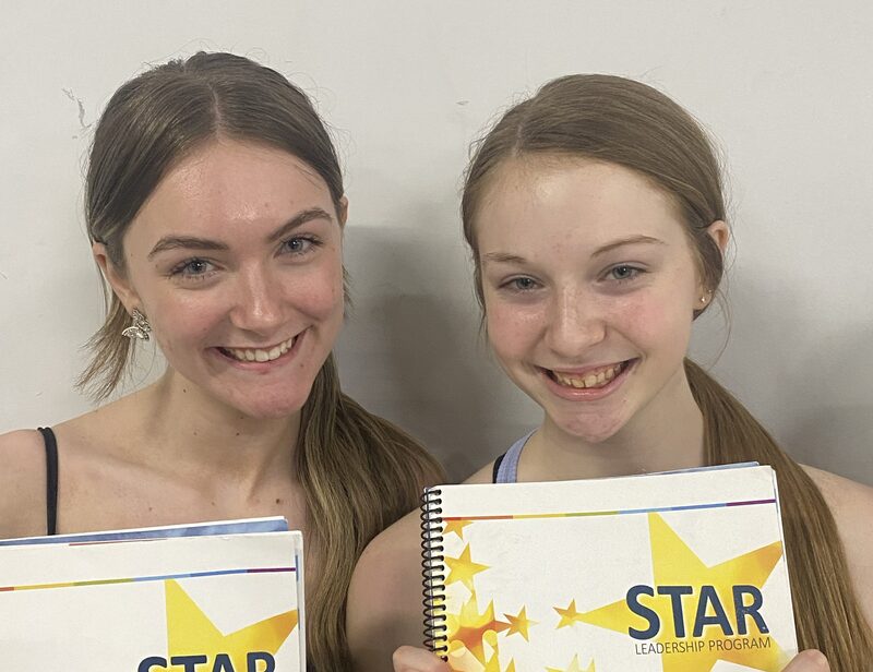 Two teenage, female students holding up copies of the Star Leadership program and smiling.