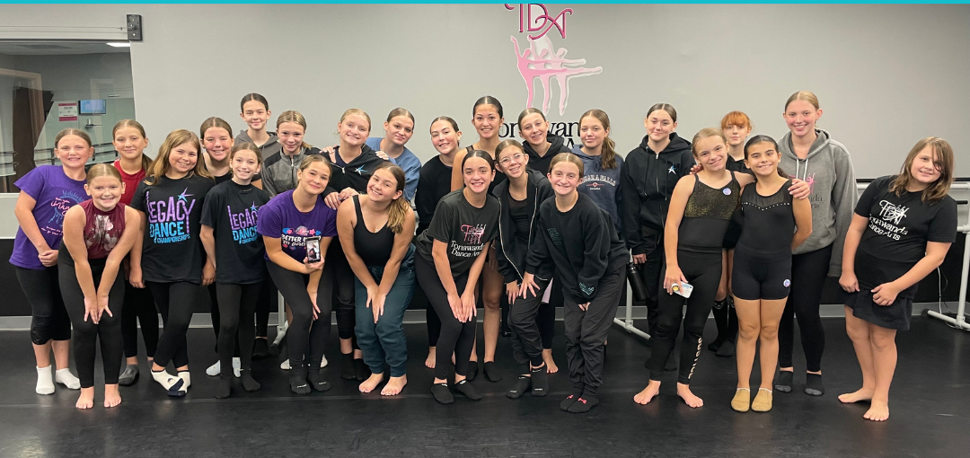 Twenty teenage female dance students posing for a group photo smiling at the camera.